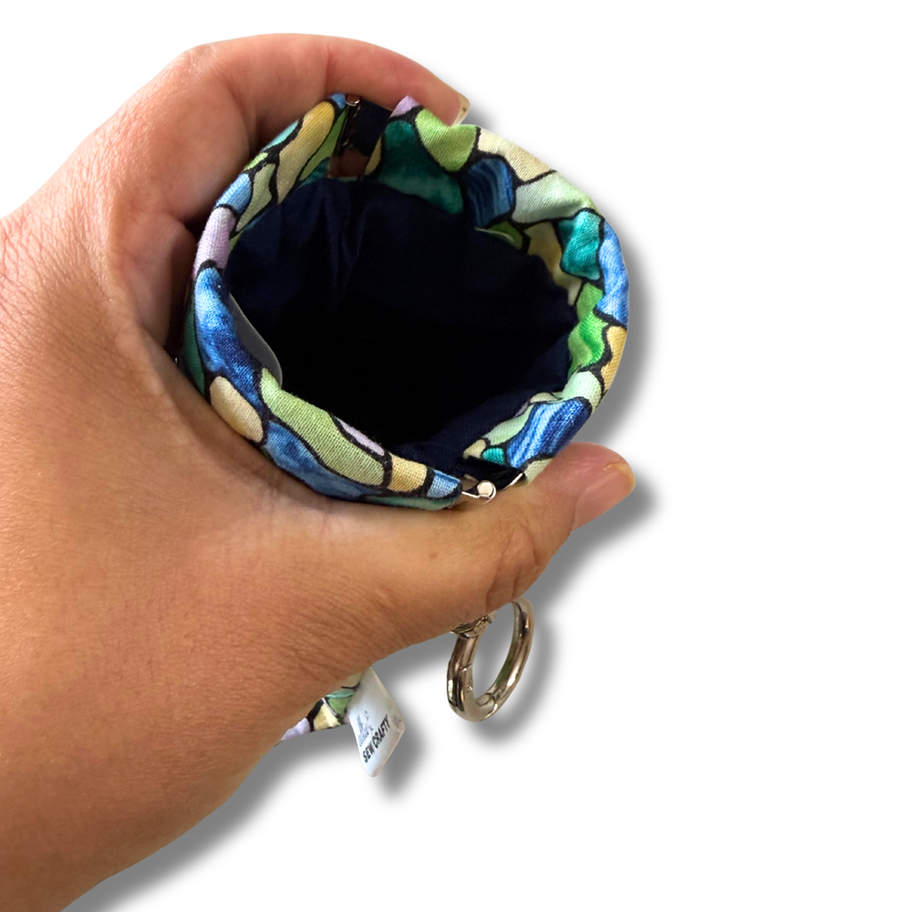 Hand holding a colorful fabric pouch with a key ring on a white background
