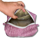 A hand is shown opening a mauve textured zippered pouch to reveal a beige interior lining with a side pocket.