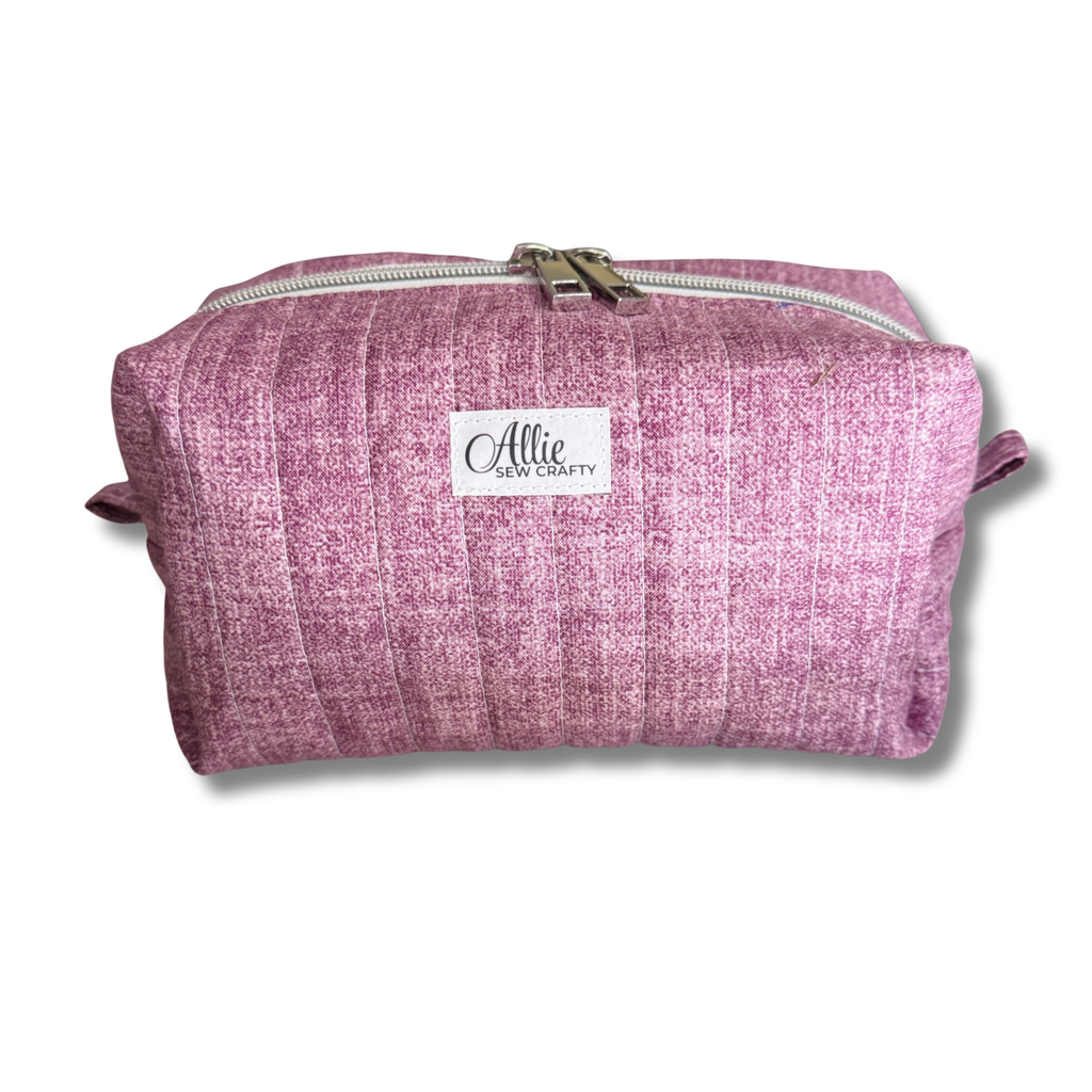 A mauve quilted fabric cosmetic pouch with a white brand label reading 'Allie Sew Crafty' on a white background.