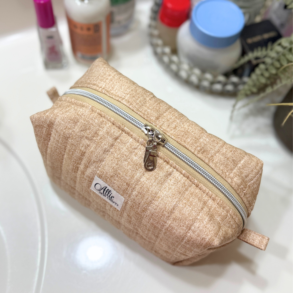 A beige quilted cosmetic pouch with a silver zipper and a small 'Allie.