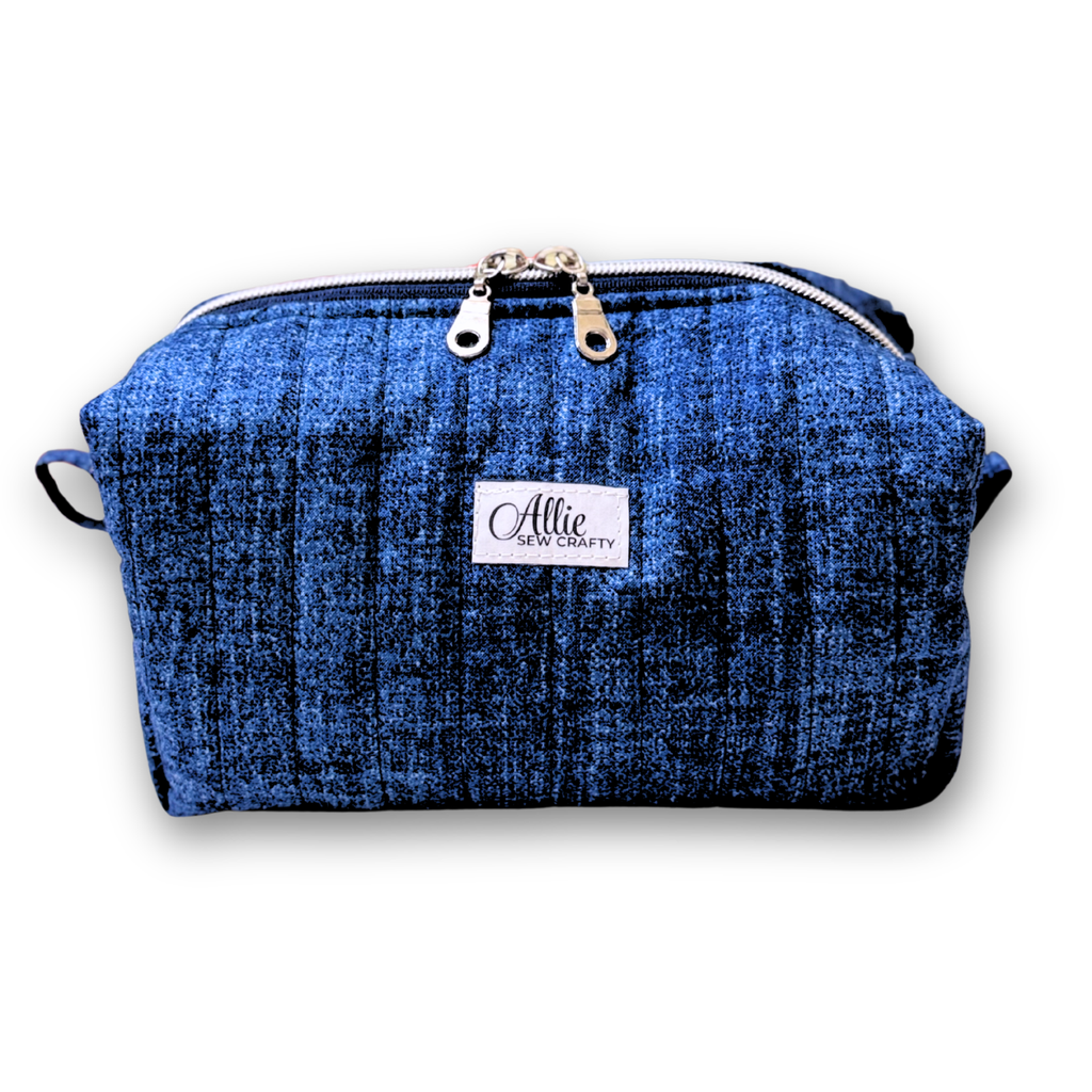A blue textured fabric cosmetic pouch with a white brand label reading 'Allie Sew Crafty' and silver zipper pulls, shown on a white background.