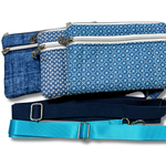 Three fabric waist bags in blue tones with different patterned designs, shown with matching shoulder straps on a white background.
