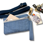 A blue and white patterned crossbody wallet shown with accessories including a phone, credit cards, keys, and a whistle on a white background.