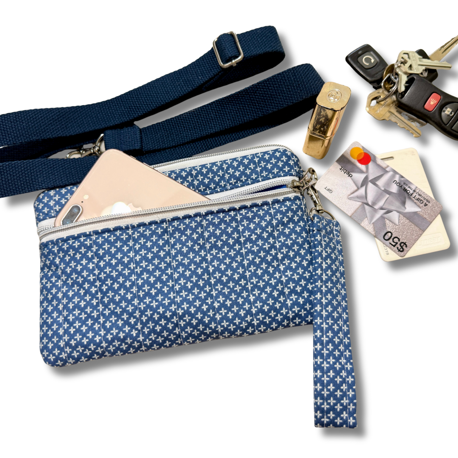 A blue and white patterned crossbody wallet shown with accessories including a phone, credit cards, keys, and a whistle on a white background.