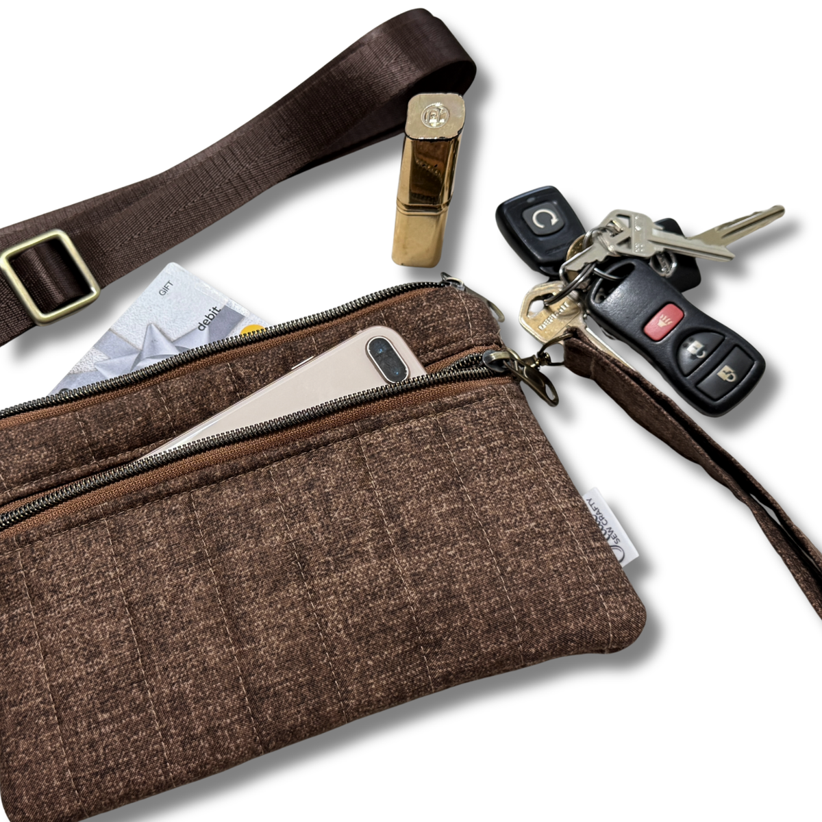 A brown textured fabric crossbody bag with a matching wrist strap, shown with a phone, card, lipstick, keys, and car key fob in its pockets on a white background.