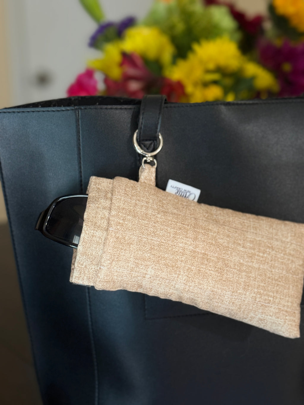 cream color pouch hanging from a black tote bag with flowers in the background