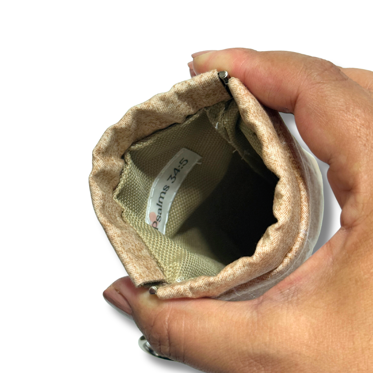 A close-up of a hand holding a beige fabric pouch or sleeve, showing the interior lining and a sewn-in label that reads 'Psalms 34:5'.