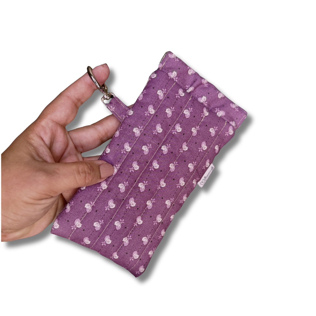 A hand holding a small purple fabric pouch with a white pattern, featuring a metal key ring attachment, against a plain white background.