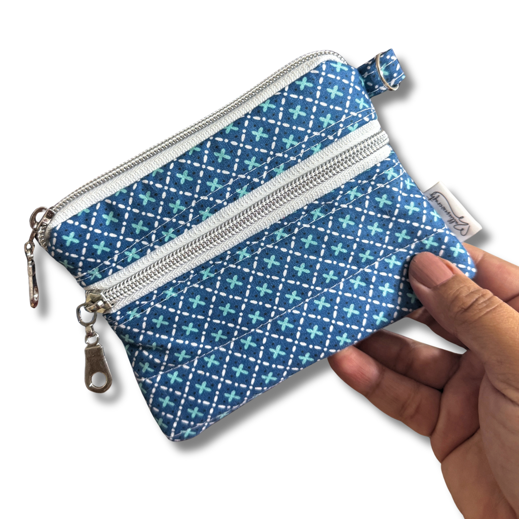 A small zippered pouch with a blue and teal geometric pattern, held by a hand against a white background.