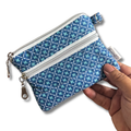 A small zippered pouch with a blue and teal geometric pattern, held by a hand against a white background.