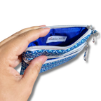 A hand holding open a small zippered pouch with a blue and white patterned exterior and a bright blue interior. A fabric label inside reads 'Psalms 34:5'.