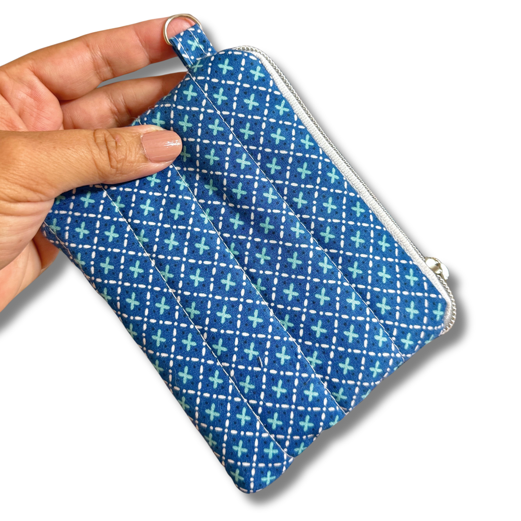 A hand holding a small zippered fabric pouch with a blue, white, and light blue geometric pattern, shown against a plain white background.
