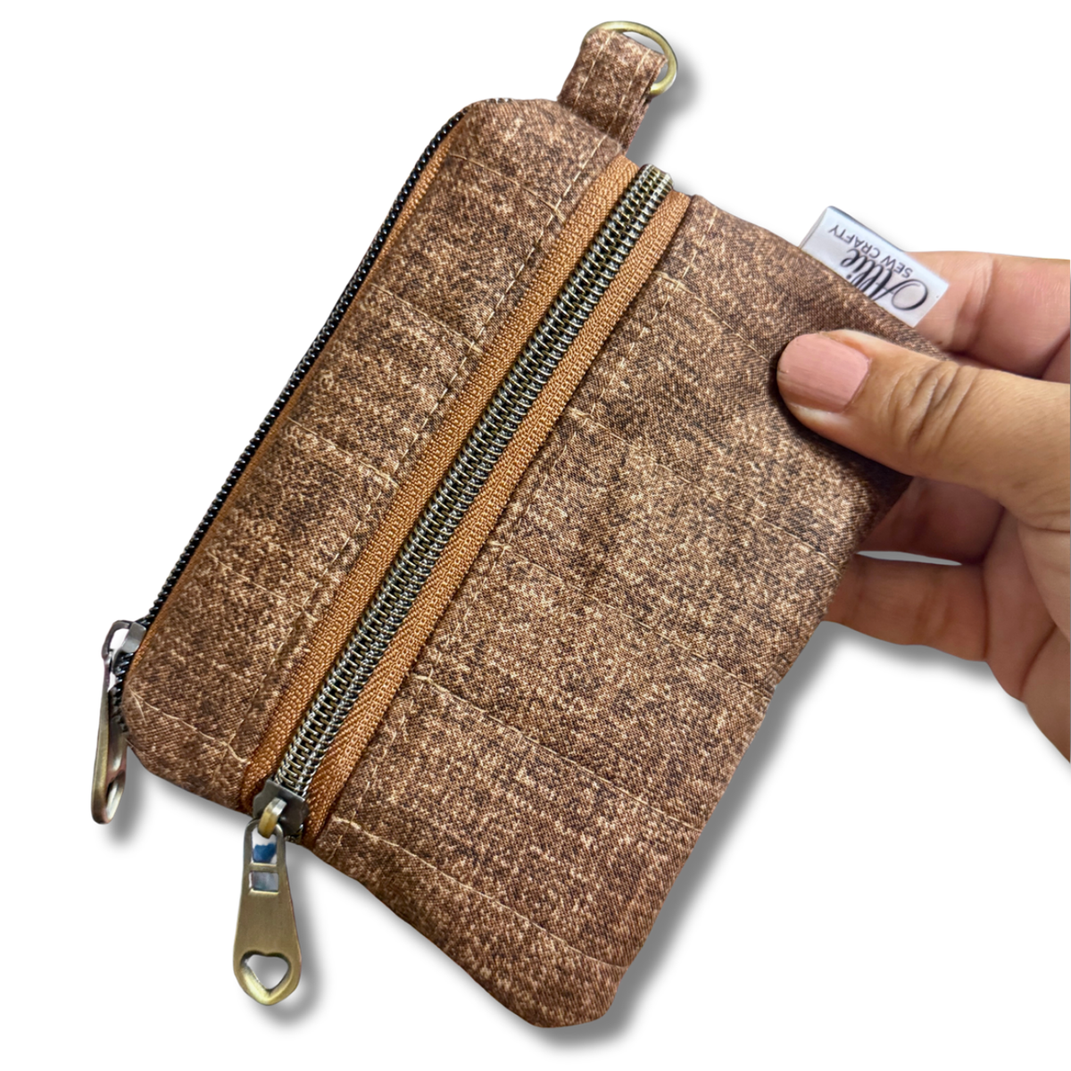 A hand holding a small brown textured zippered pouch with a gold-tone zipper and pull tab, shown against a plain white background.