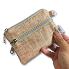 A small zippered coin pouch in a textured beige fabric, held by a hand against a plain white background. The pouch features a silver zipper, a small metal ring, and a white fabric tag with the brand name 'Allie Sew Crafty'.