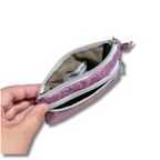 A hand holding open a small zippered pouch with a textured pink exterior and a beige interior lining, shown against a plain white background.
