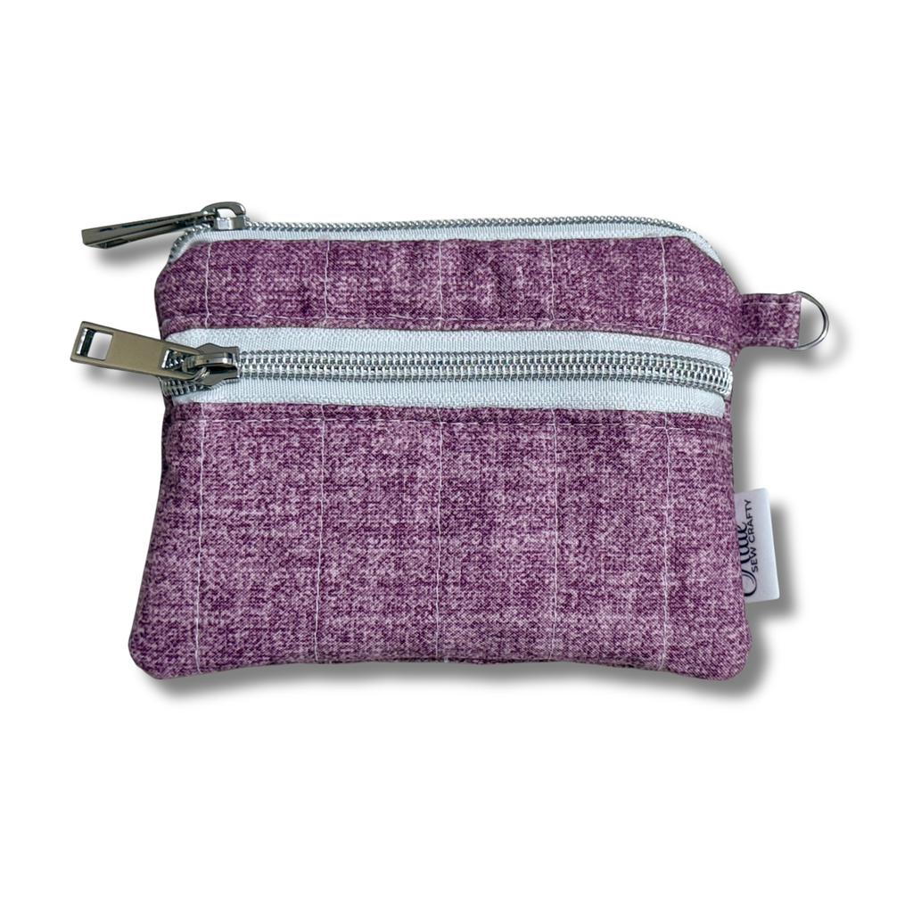 A small purple woven fabric zippered pouch with two silver metal zippers and a small white brand tag on the side, shown on a white background.