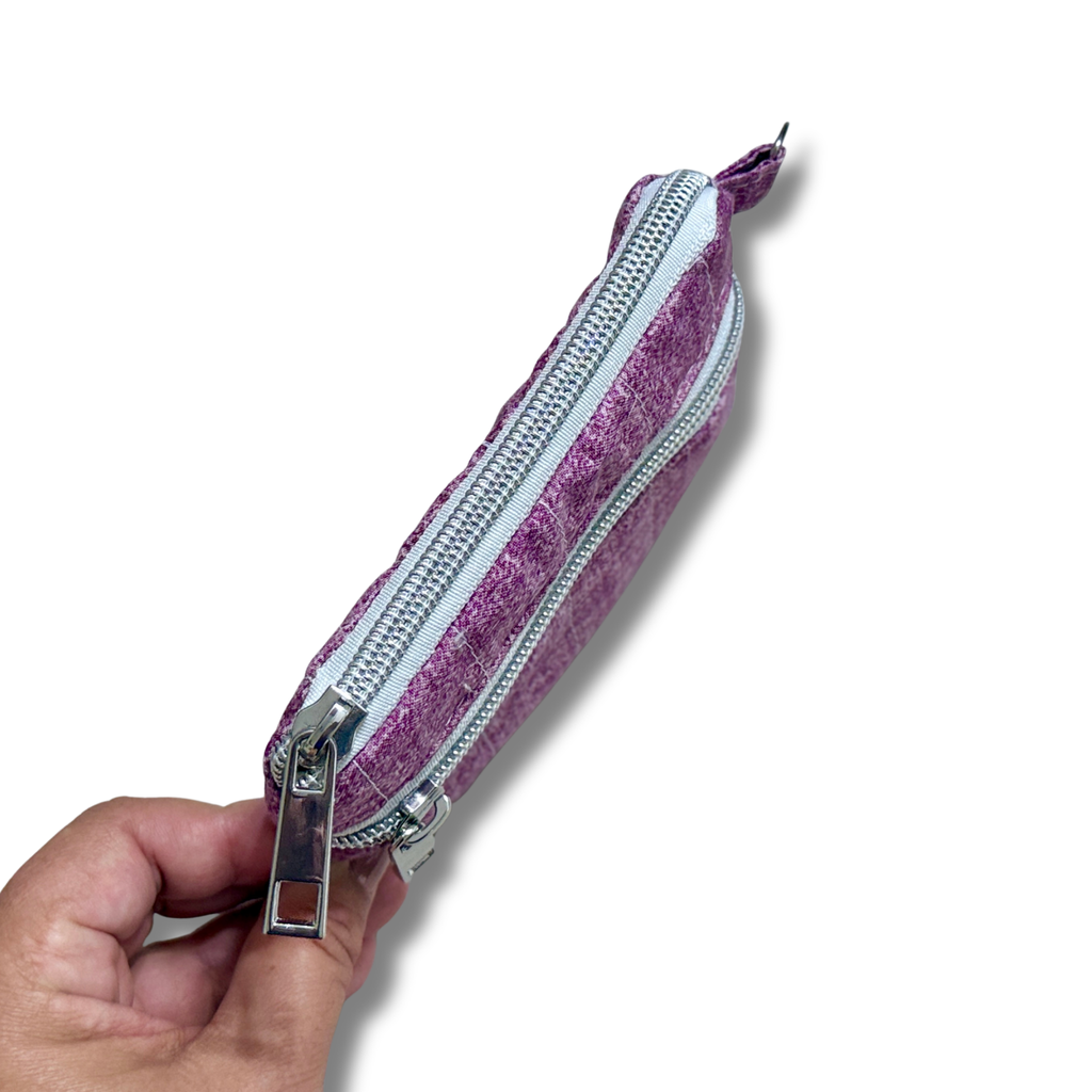 A hand holding a small zippered pouch with a purple and white striped patterned fabric and silver metal hardware, shown against a plain white background.