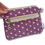 A purple quilted fabric wallet with a white floral pattern, featuring two zippered compartments, a card slot, and a keychain attachment with keys and a car key fob. 