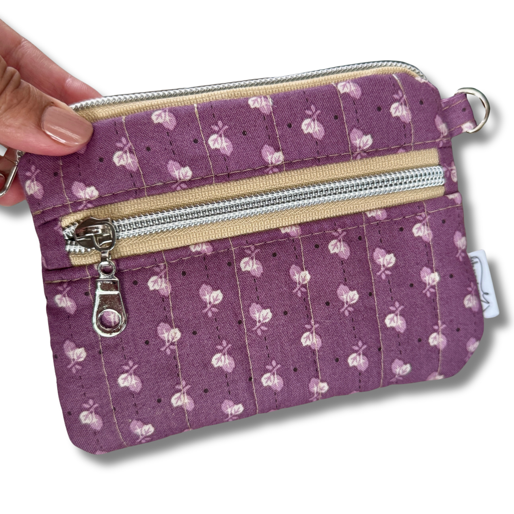 A purple quilted fabric wallet with a white floral pattern, featuring two zippered compartments, a card slot, and a keychain attachment with keys and a car key fob. 