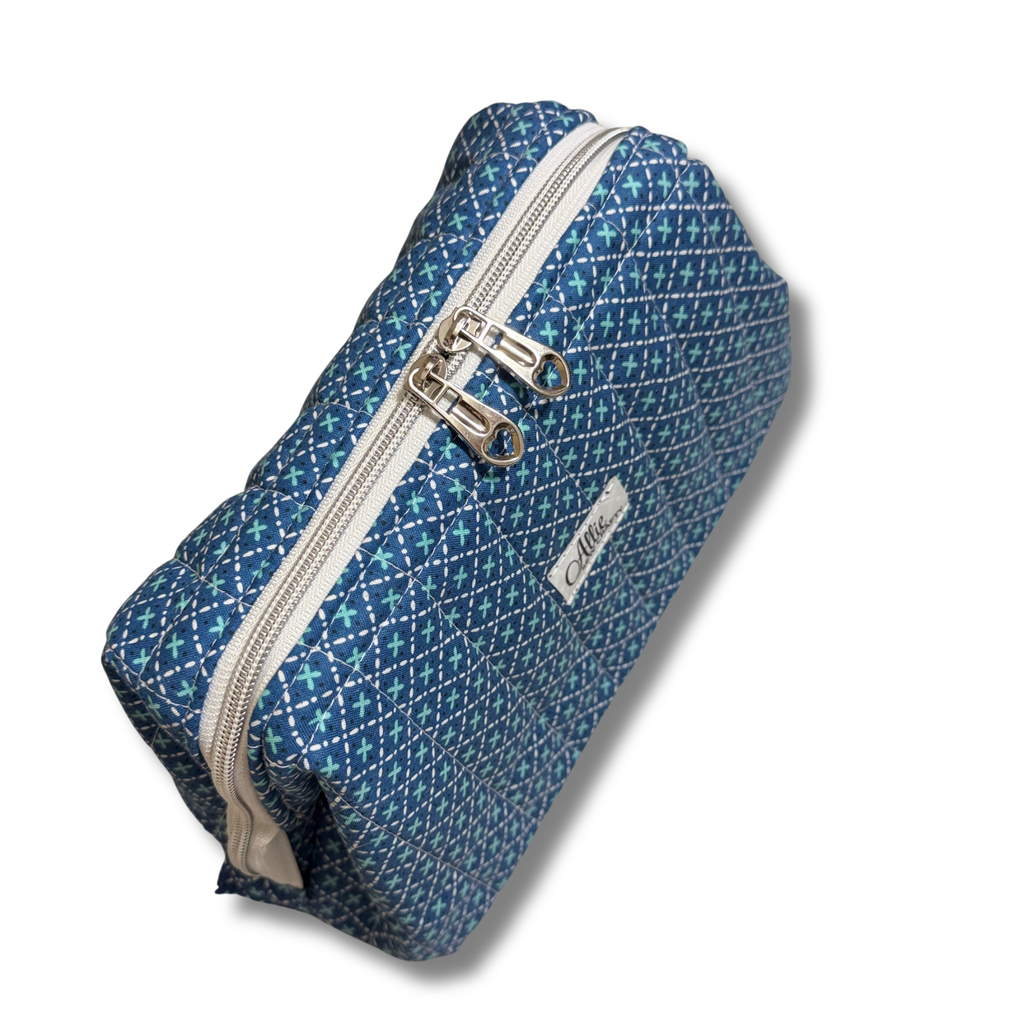 A blue patterned zippered pouch with silver zipper pulls and a small white brand label, photographed on a clean white background.