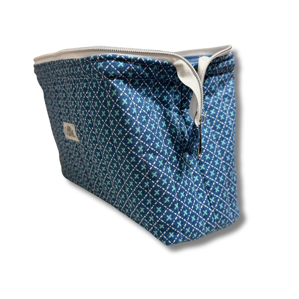 A rectangular zippered pouch with a blue and teal geometric pattern, featuring a white zipper and a small fabric brand label on the side, set against a plain white background.