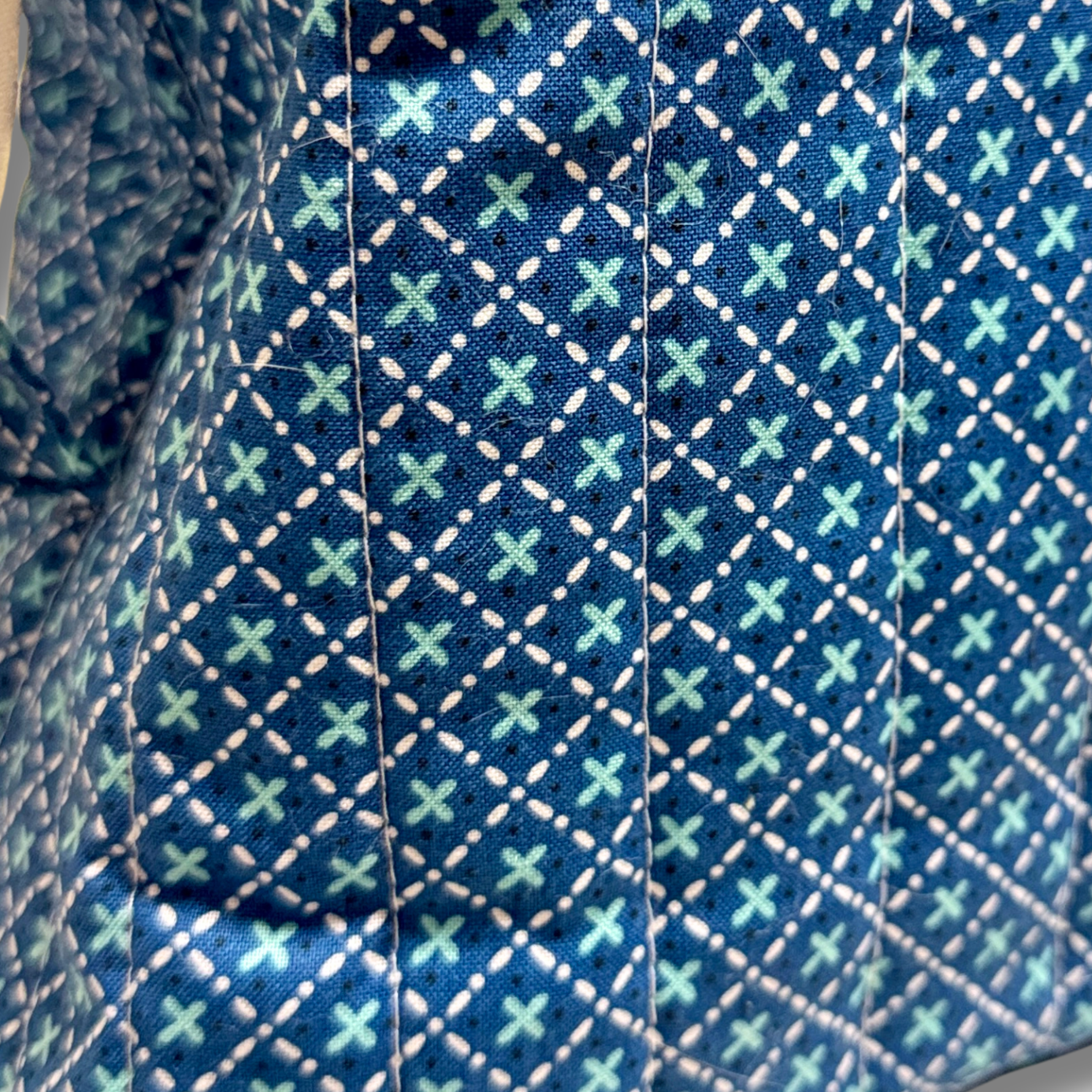Close-up of a patterned fabric with a dark blue base, white dashed diamond lines, and small mint green crossed-stitch style motifs.