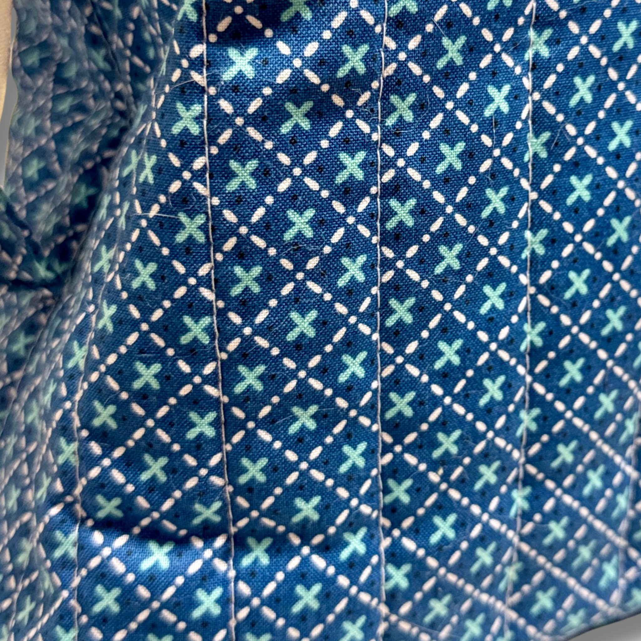 Close-up of a patterned fabric with a dark blue base, white dashed diamond lines, and small mint green crossed-stitch style motifs.