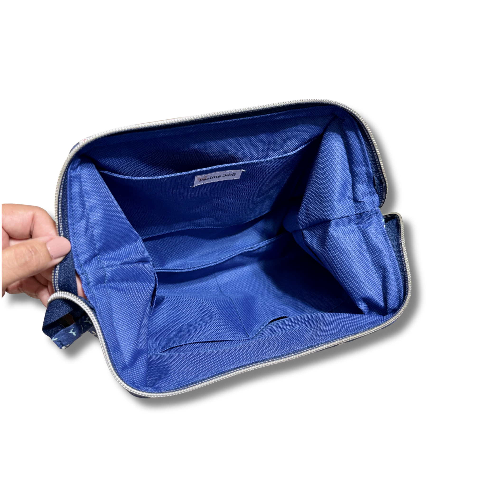 A blue zippered pouch or organizer shown open, with a hand holding the left side to display the interior compartments and lining. The pouch has a silver zipper and a small interior label.