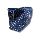 A navy blue quilted cosmetic pouch with a white and pink floral pattern, featuring a silver zipper and a small white brand label on the side.