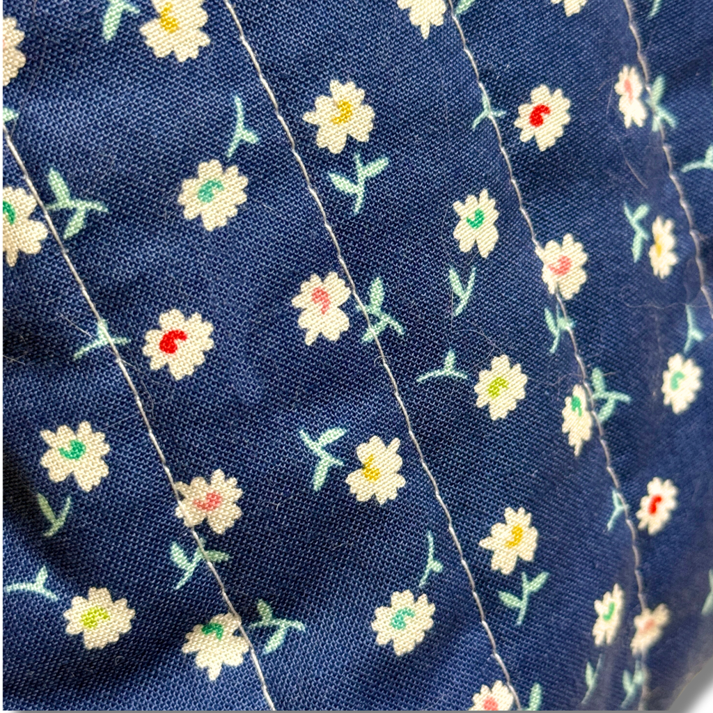 Close-up of a navy blue fabric with a repeating pattern of small white daisies and tiny colorful floral details, stitched vertically.