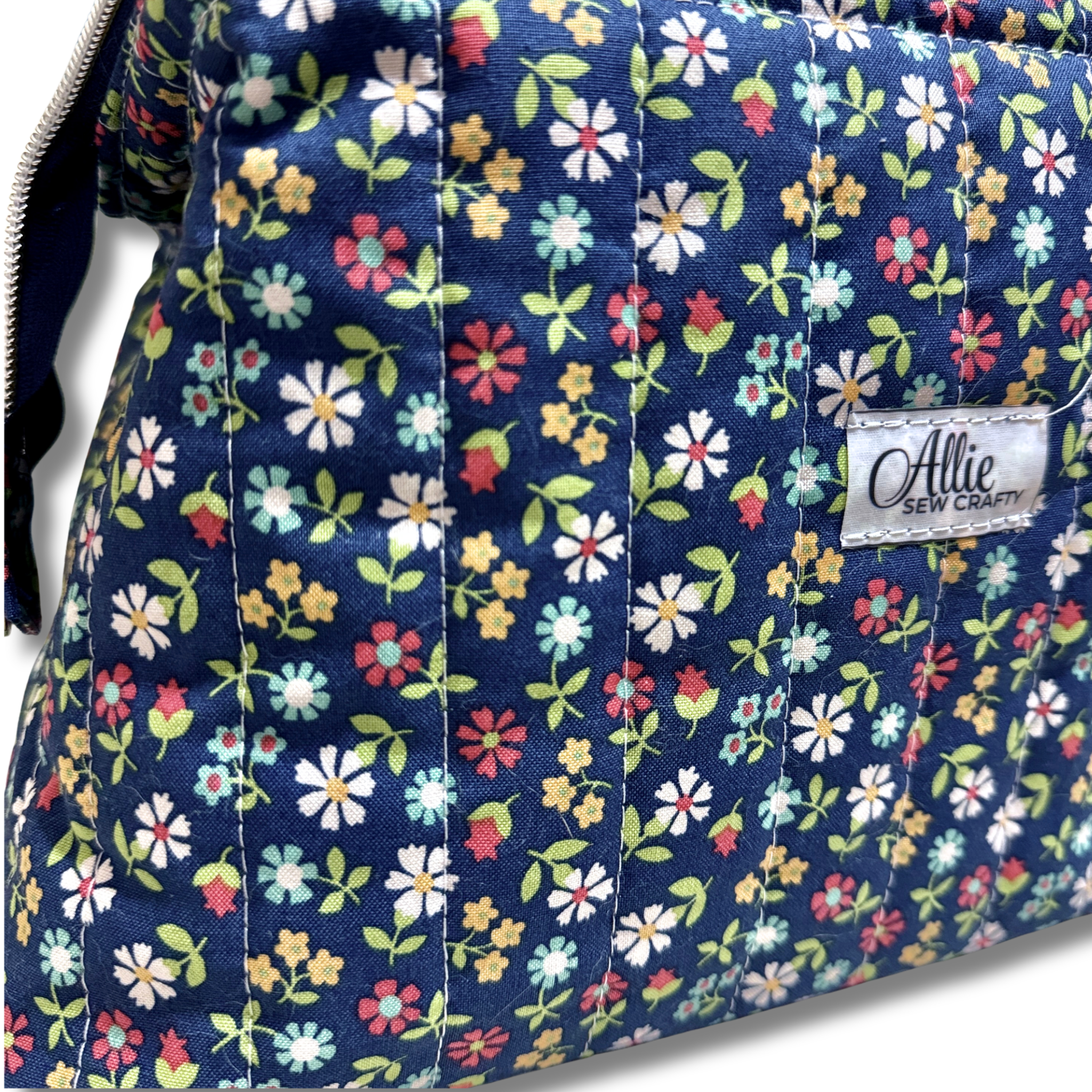 close up of quilting cotton fabric navy blue background with a colorful floral pattern of pink, yellow, white, and green flowers and Allie Sew Crafty in a white label.