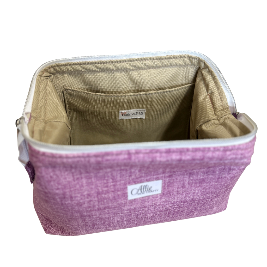 A rectangular zippered cosmetic bag in a heathered purple fabric, shown open to reveal a beige interior lining with a front pocket. A white brand label reading 'Allie.