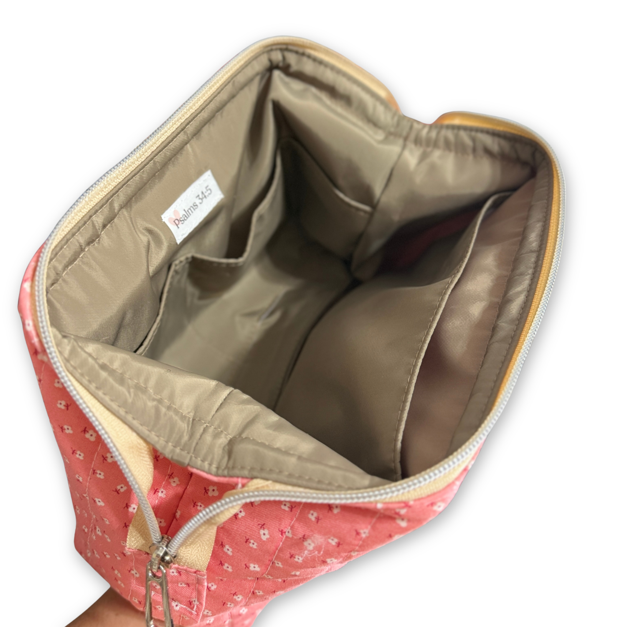 Pink quilted cosmetic bag with a floral pattern, shown open to display the beige interior lining and zippered compartments. A brand label reading 'Psalms 34:5' is visible inside.