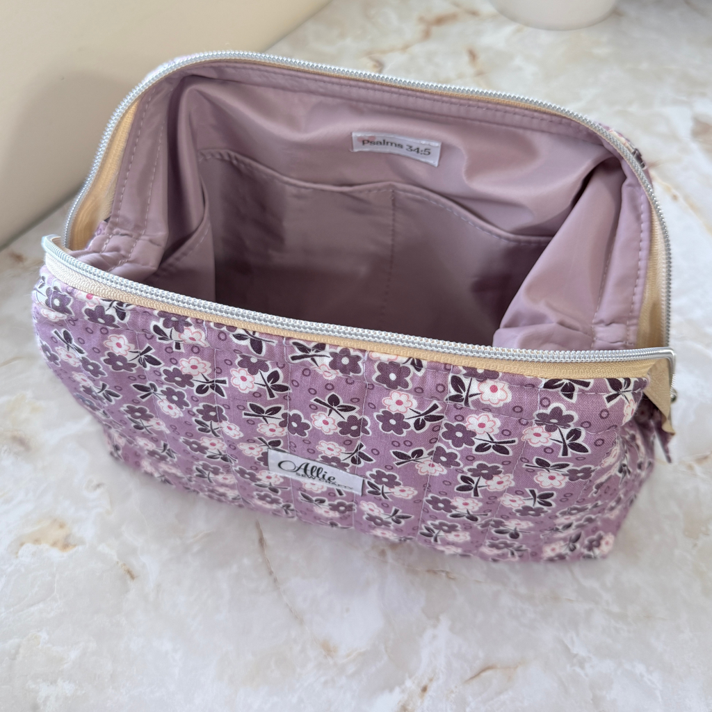 Opened Purple floral Full View Pouch to show the lavender water-resistant interior lining, interior pocket, and Psalm 34:5 tag