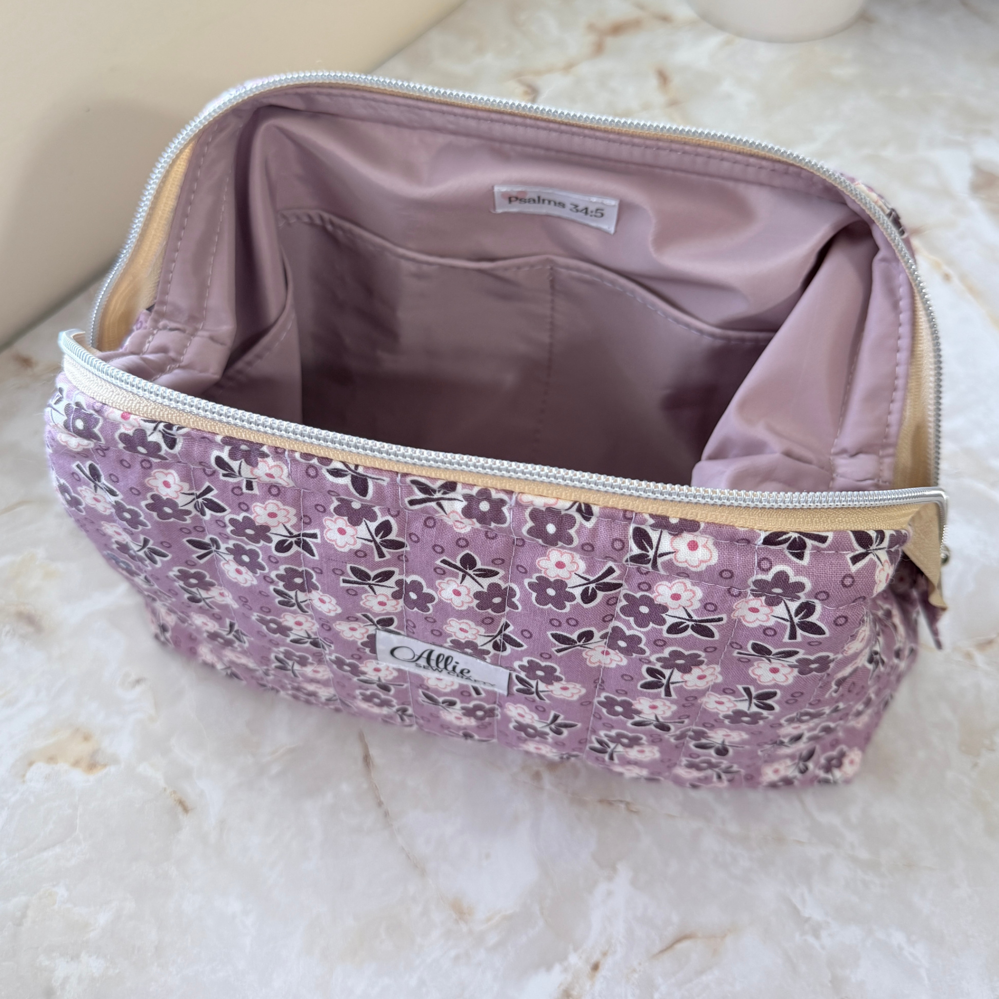 Opened Purple floral Full View Pouch to show the lavender water-resistant interior lining, interior pocket, and Psalm 34:5 tag