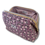 A lavender quilted cosmetic pouch with a floral print, shown open to reveal a light purple interior. The pouch features a purple, white, and black floral pattern, a silver zipper, and a brand label reading 'Allie'.