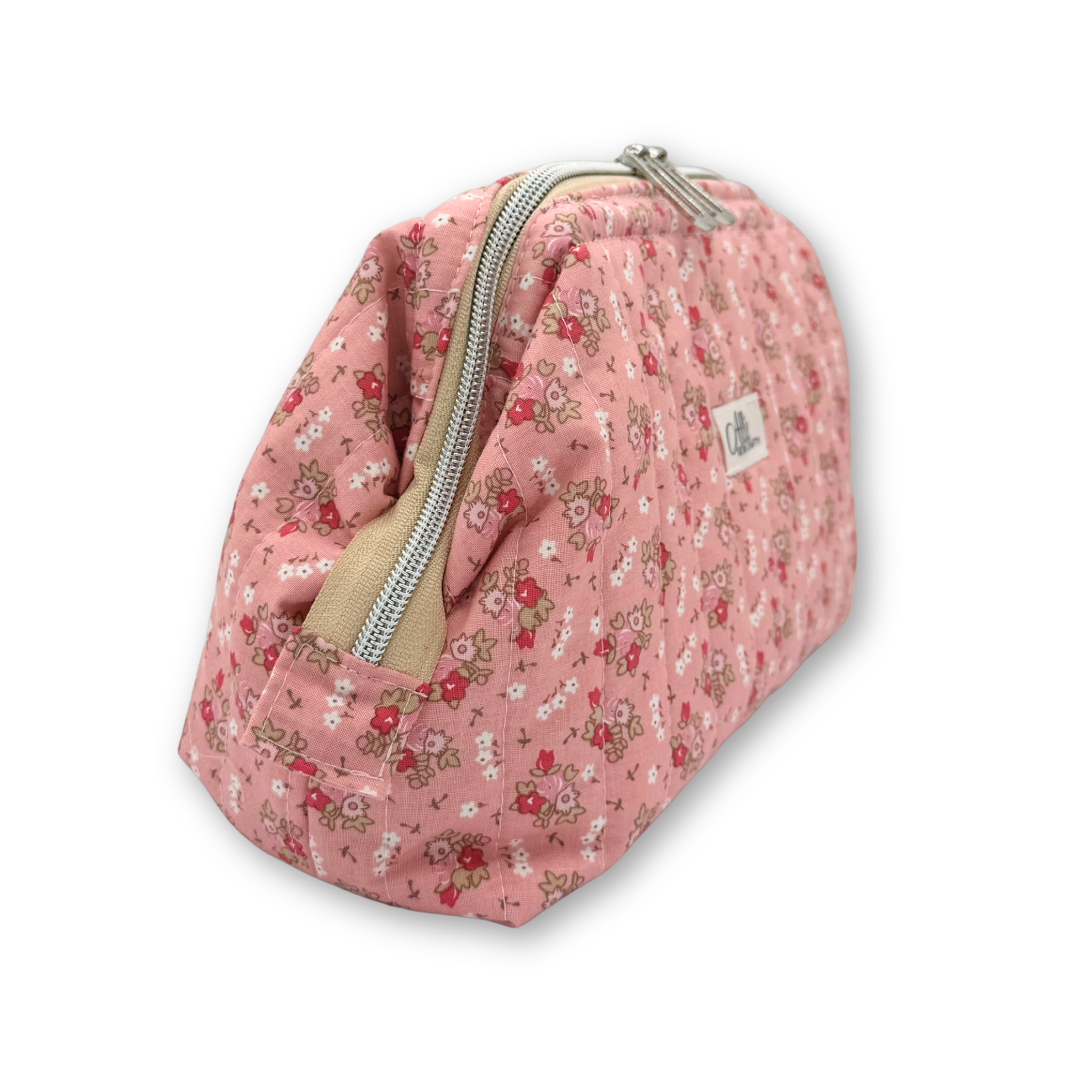A pink quilted cosmetic pouch with a delicate red, white, and green floral print, featuring a silver zipper and a small white brand label. Angled view