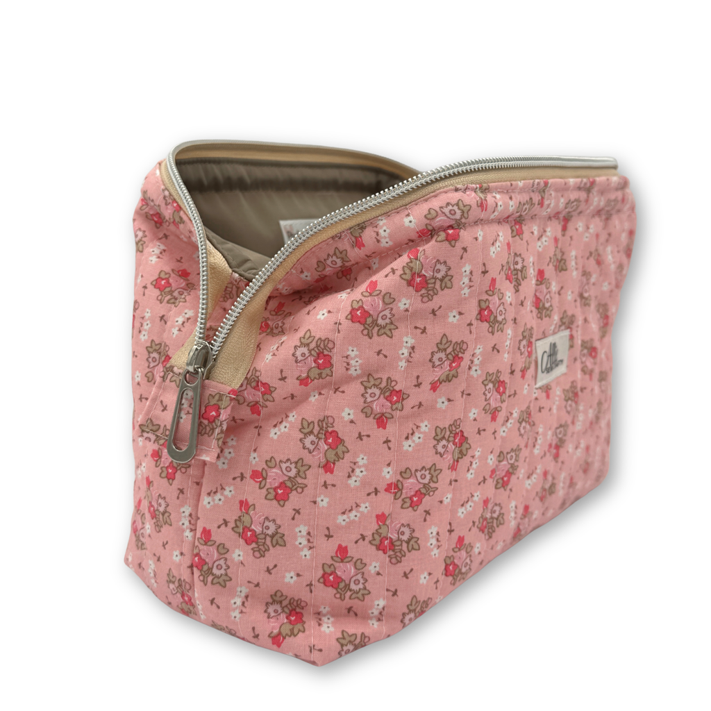 A pink zippered cosmetic pouch with a small-scale floral, featuring a silver zipper and a small brand label on the side.