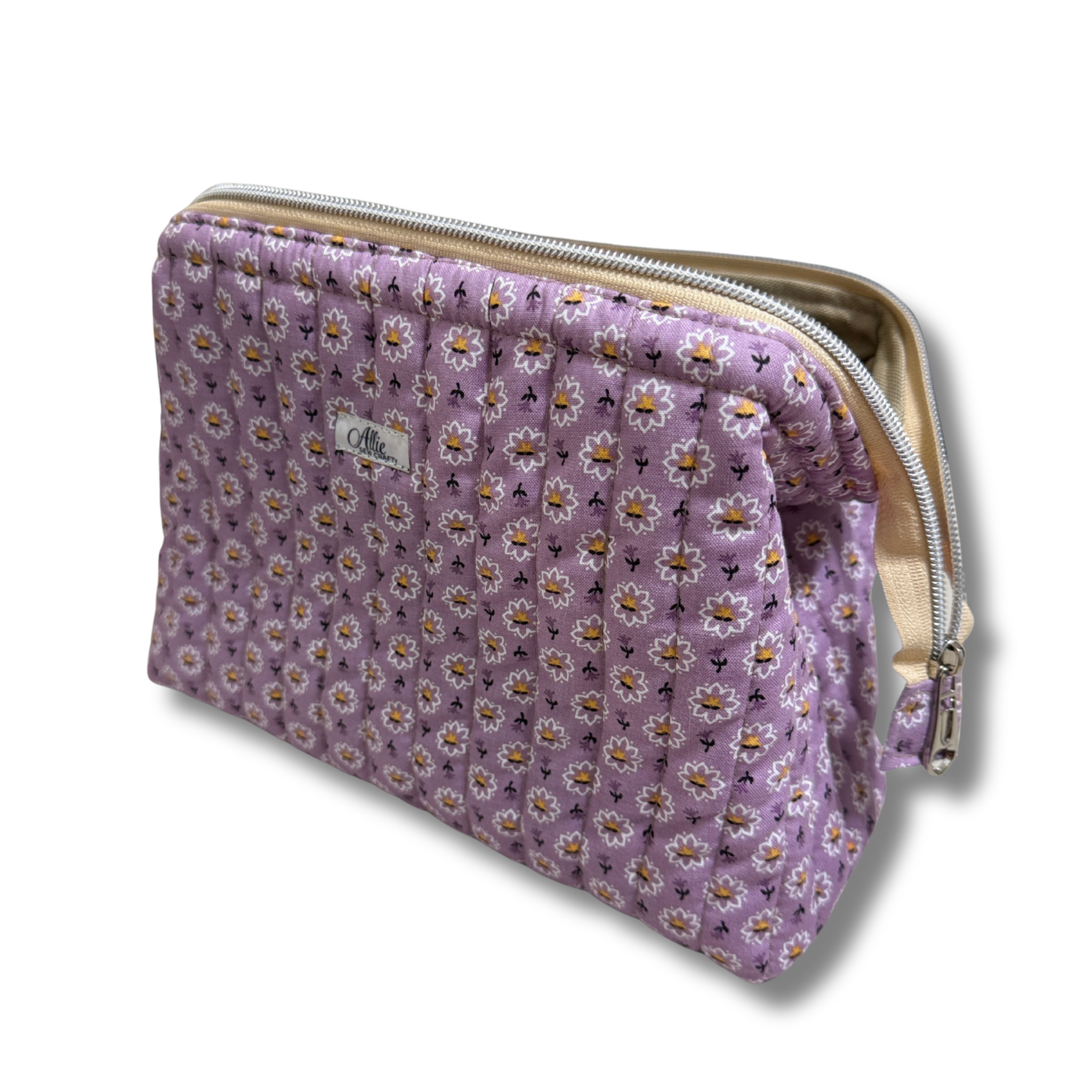 A quilted lavender cosmetic pouch with a daisy floral pattern, featuring a cream zipper and a small white label 'Allie Sew Crafty' brand label.