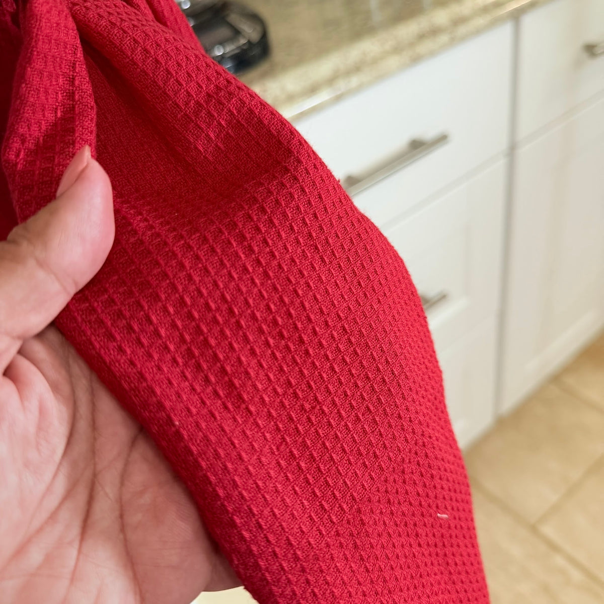 Red textured fabric held by a hand with a kitchen background